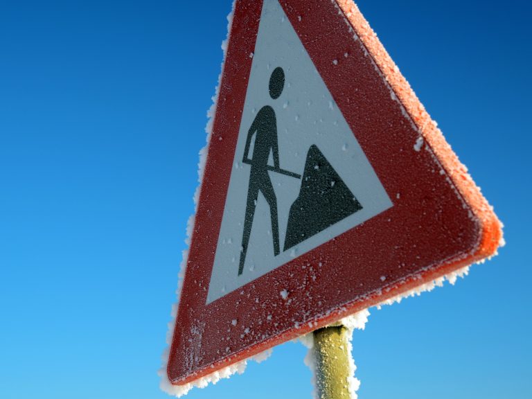 Close-up of a frosty road construction sign with a vibrant blue sky background.